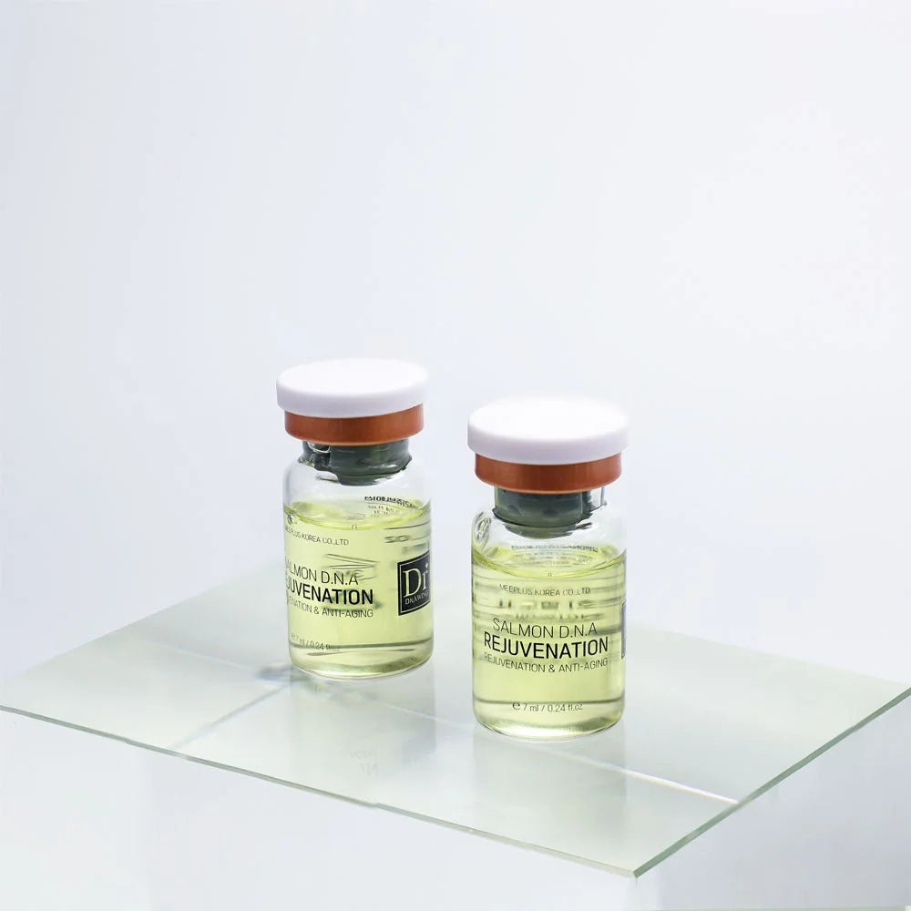 Two small glass vials with white caps and orange bands, containing a pale yellow liquid, displayed on a clear glass platform against a white background. The labels read 'REJUVENATION' and show the Dermalogics brand.